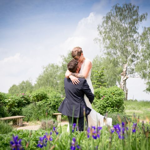Hochzeitspaar umarmt sich in grüner Landschaft vor blau-weißem Himmel