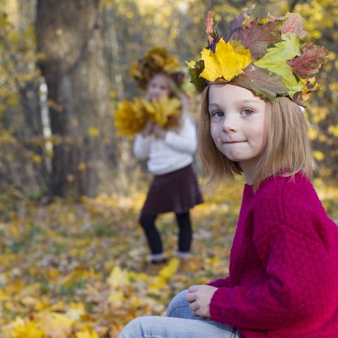 Mädchen im roten Pullover mit Krone aus Herbstlaub im herbstlichen Wald