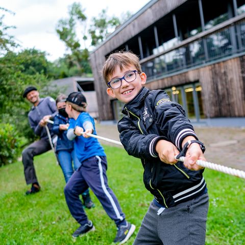 Zwei Jungen und ein Erwachsener beim Tauziehen vor Natur-Erlebnishaus