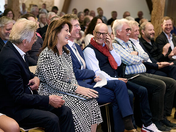 Mehrere Herren und eine Dame sitzen in der ersten Reihe bei einer Veranstaltung