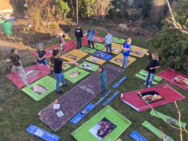 Eine Gruppe von Kindern auf einer Rasenfläche wird angeleitet, Planen mit Essensmotiven zu sortieren