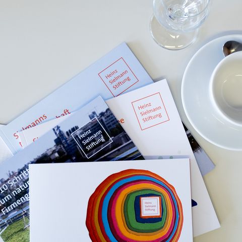 Blick aus der Vogelperspektive auf drei Broschüren Heinz Sielmann Stiftung, Kaffeetasse und Glas auf weißem Tisch