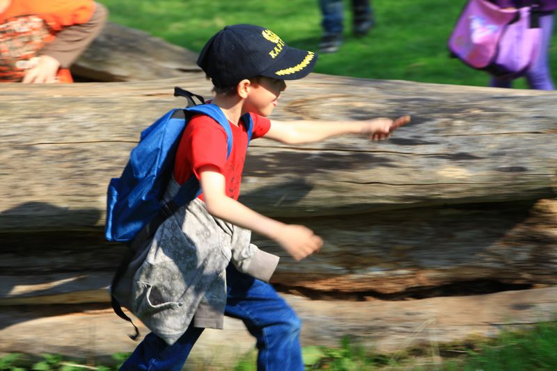 Junge mit Rucksack und Basecap läuft an Baumstamm entlang