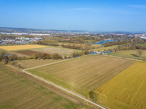 Die Biotoplandschaft am Flüthewehr in Göttingen vor den umgesetzten Maßnahmen. Aus der Vogelperspektive sieht man die noch intensiv genutzte Ackerfläche. Links und rechts sind weitere intensiv genutzte Ackerflächen. Am Horizont befinden sich einige Gebäude der Stadt Göttingen. Die Leine fließt durch dieses Areal.
