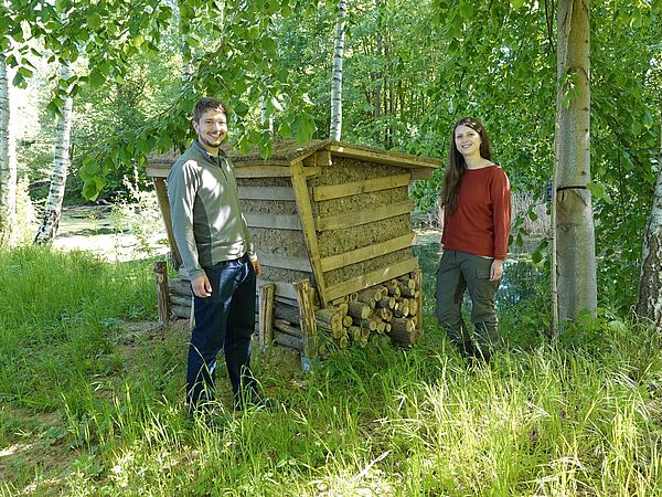 Eisvogel-Nisthilfe am Beuster Teich Junger Mann und Frau stehen von zwei Seiten neben einer Nisthilfe aus Holz