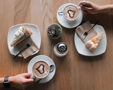 Café GUT(e) auszeit: Zwei Teller mit Tortenstück, Kaffeetassen, Zucker, Hände