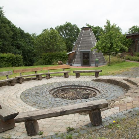 Runde Feuerstelle an der Dachsburg mit Köhlerhütte im Hintergrund