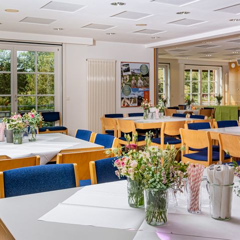 Raum Bussard: Tische mit Blumen in Vasen und Tischdecken und Holzstühlen mit blauen Bezügen