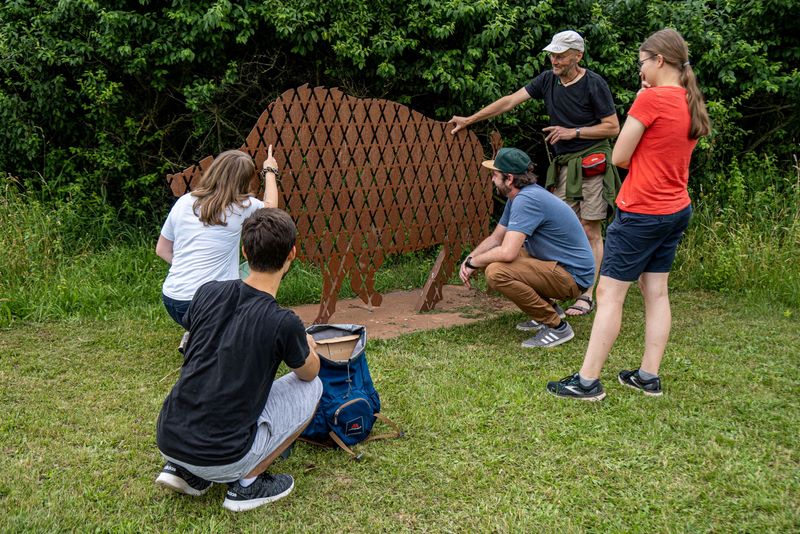 Outdoor Escape Game: Fünf Personen hockend und stehend betrachten Wildschwein-Skulptur auf Grasfläche